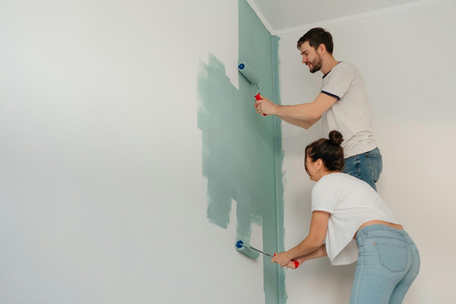Un jeune couple travaille ensemble à la peinture d'un mur au rouleau, illustrant le travail d'équipe et l'amélioration de l'habitat.